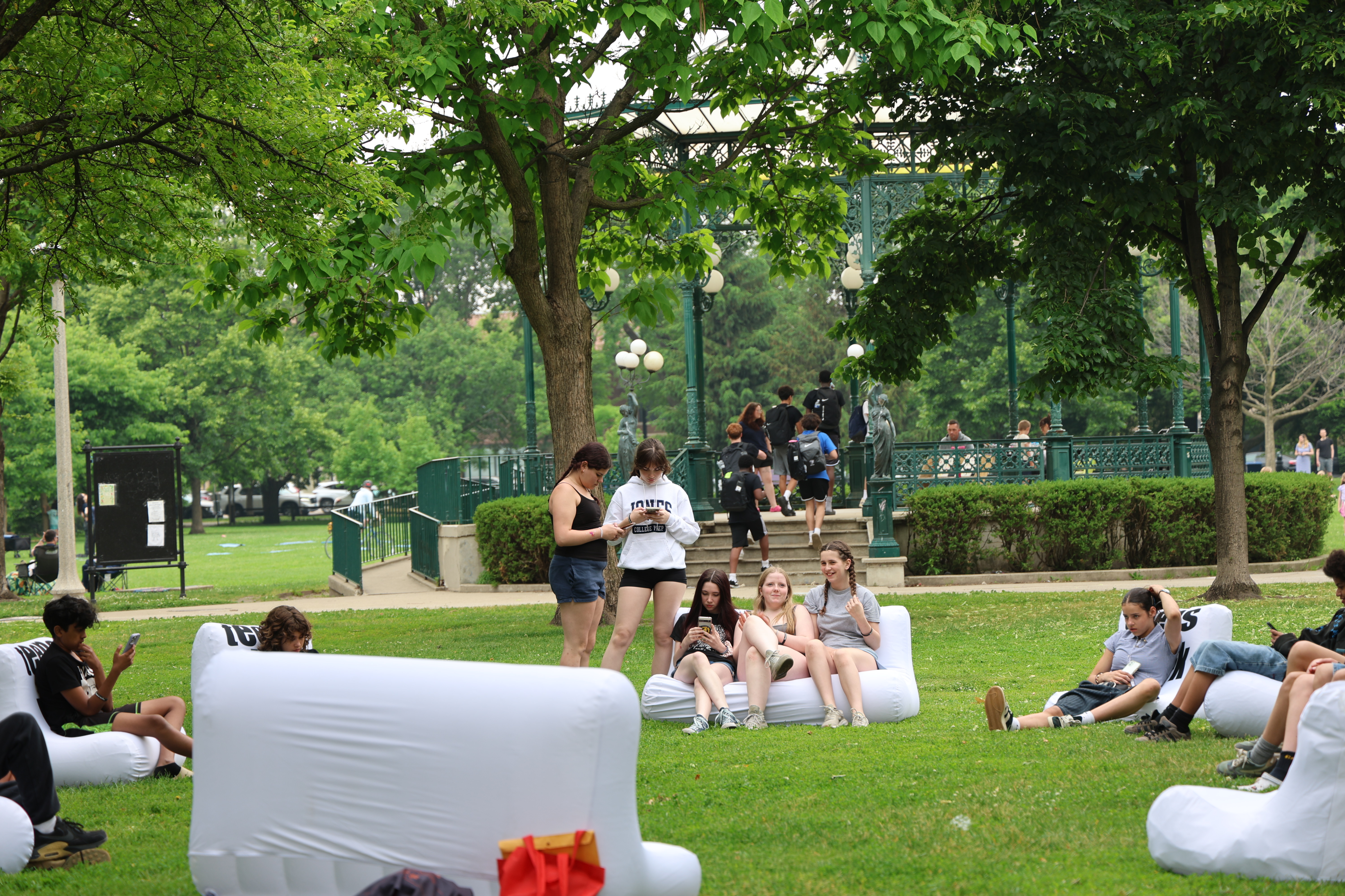 People relax on inflatable couches in a park. A gazebo is visible in the background.
